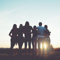 Young people standing together at sunset, arms around each other