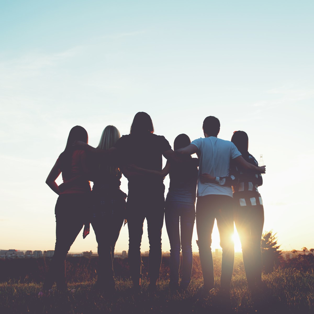 Young people standing together at sunset, arms around each other