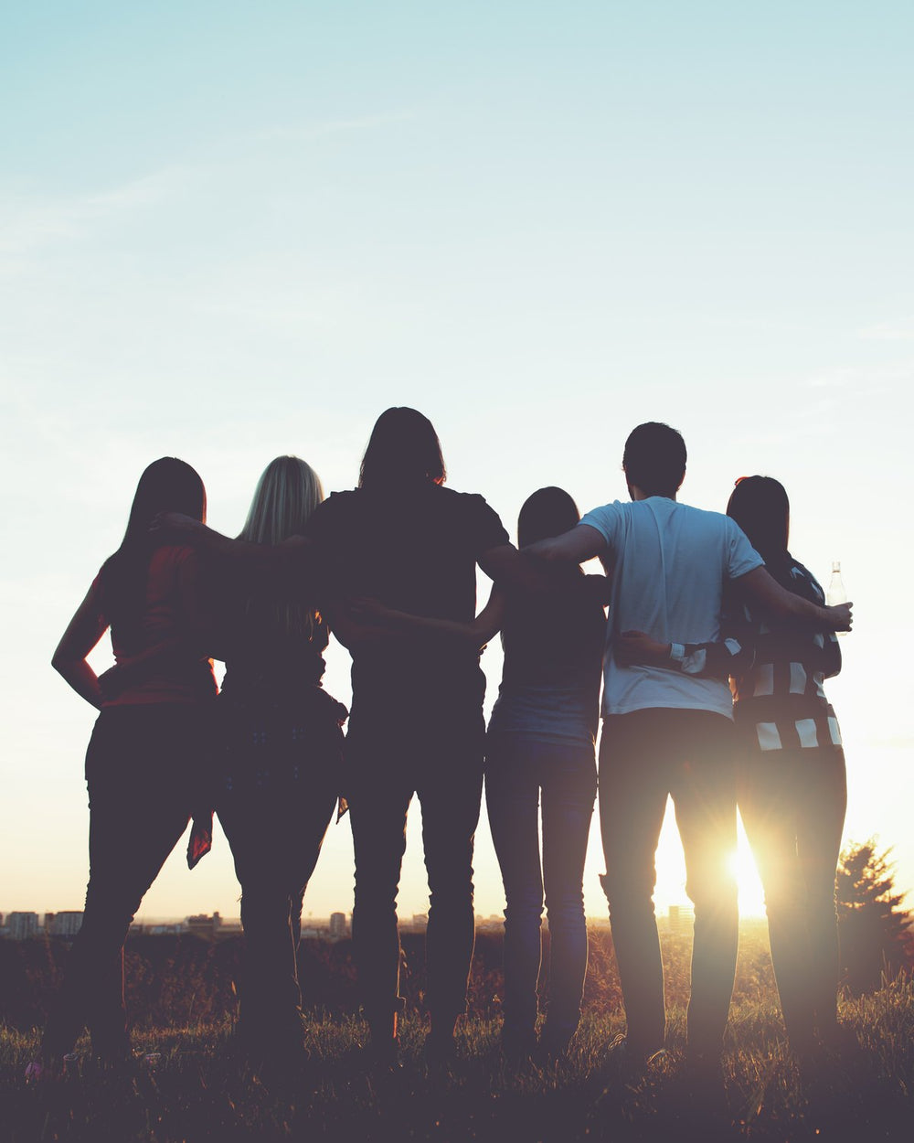 Young people standing together at sunset, arms around each other